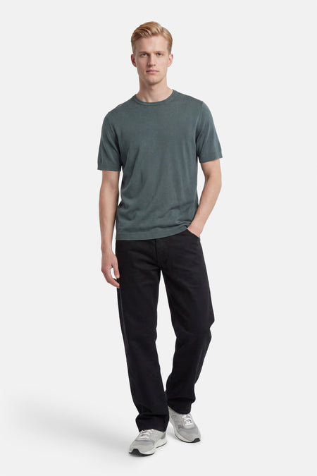 Groene pull met ronde hals en korte mouwen van SELECTED, gedragen door een man met zwarte jeans en grijze sneakers.