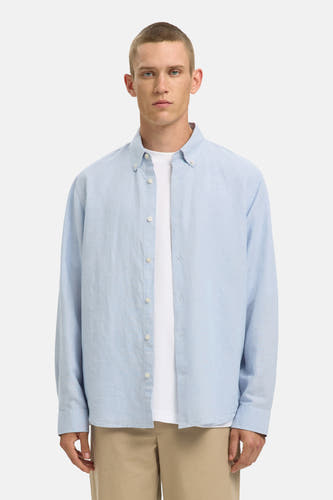 Chemise bleue à manches longues de SELECTED, portée sur un t-shirt blanc, avec un pantalon beige et des mocassins en cuir.