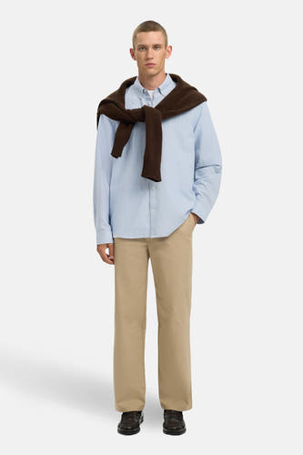 Chemise bleue à manches longues de SELECTED, avec un pull marron noué sur les épaules et un pantalon beige.