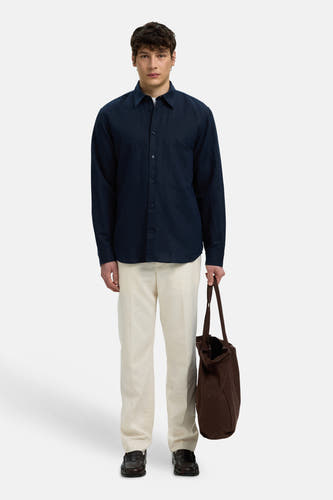 Blauw hemd met lange mouwen van SELECTED, gedragen door een man met een crème broek en bruine tote bag.