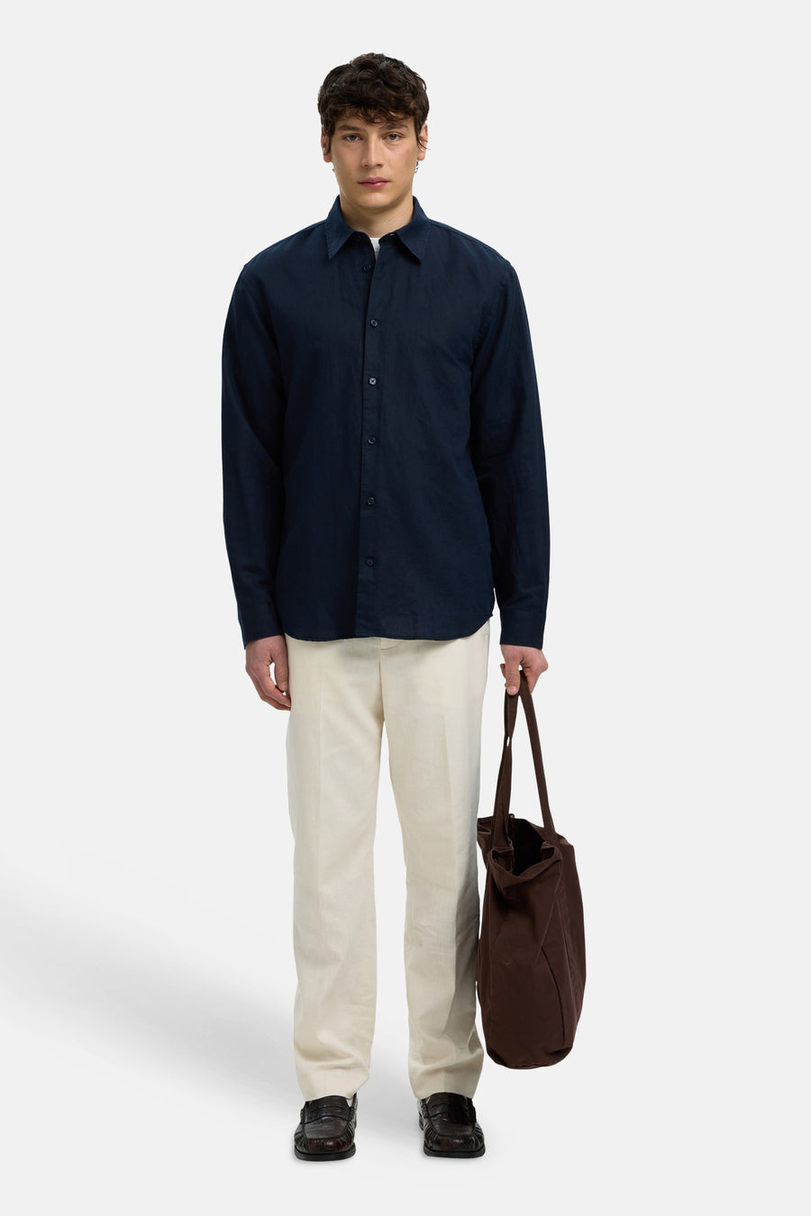 Blauw hemd met lange mouwen van SELECTED, gedragen door een man met een crème broek en bruine tote bag.