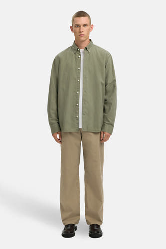 Groen overhemd met lange mouwen van SELECTED, met witte knoopsluiting, gedragen over een wit T-shirt en beige broek.
