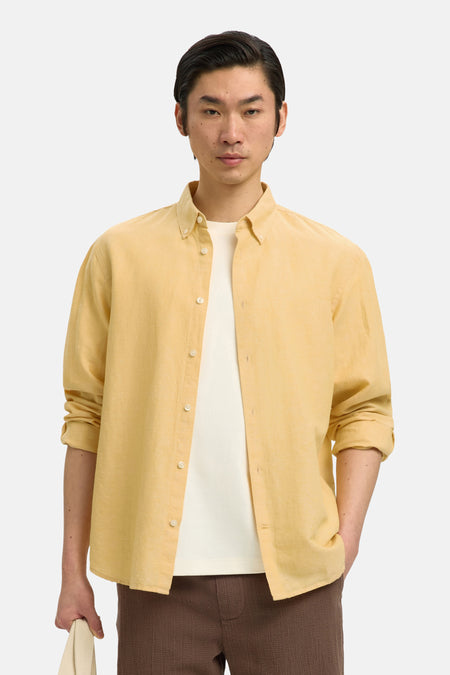 Chemise jaune de SELECTED, portée avec un t-shirt blanc, un short marron, des sandales et un sac écru.