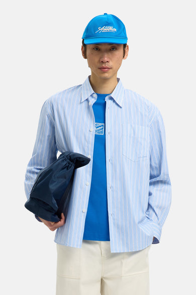 Chemise rayée bleue de SELECTED, portée sur un t-shirt bleu, avec un sac bleu marine en bandoulière.