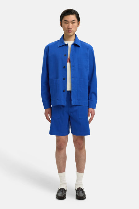 Blauwe short van SELECTED, gecombineerd met een blauw jasje, witte sokken en bruine schoenen.
