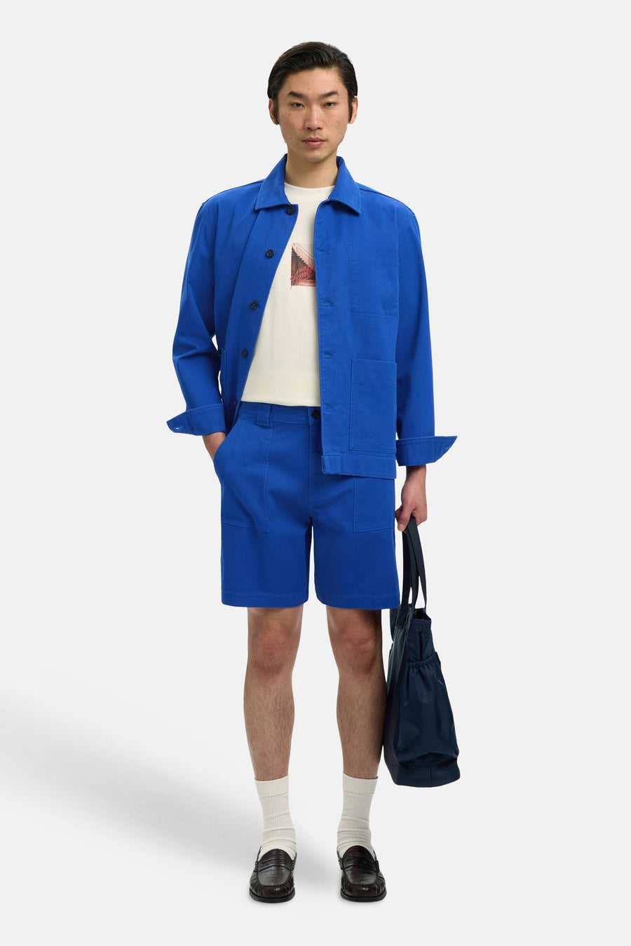 Short bleu de SELECTED, avec poches et porté avec un t-shirt blanc, une chemise bleue et des chaussures en cuir.