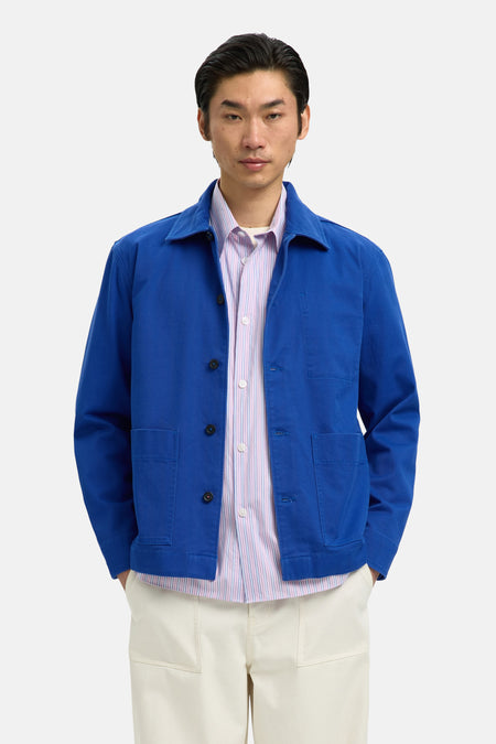Manteau bleu de SELECTED, porté sur une chemise rayée et un pantalon crème, avec des chaussures marron.