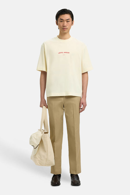 T-shirt écru de SELECTED, avec imprimé texte rouge, porté avec un pantalon kaki et un sac clair.