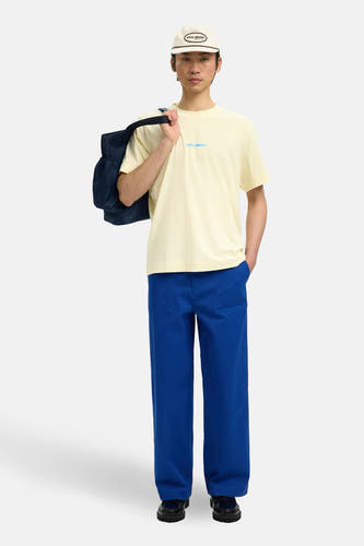T-shirt écru (manches courtes) de SELECTED, avec un texte bleu, porté avec un pantalon bleu et une casquette.