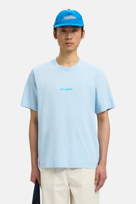 Blauw T-shirt van SELECTED, met een klein logo op de borst, gedragen met een blauwe pet en crèmekleurige broek.
