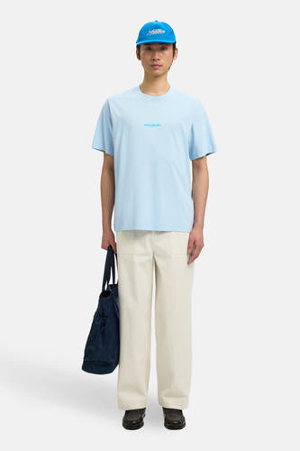 T-shirt bleu à manches courtes de SELECTED, avec petit imprimé texte et combiné avec une casquette, un pantalon beige et un sac.