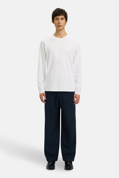 Wit T-shirt met lange mouwen van SELECTED, gedragen met donkerblauwe broek en zwarte loafers.
