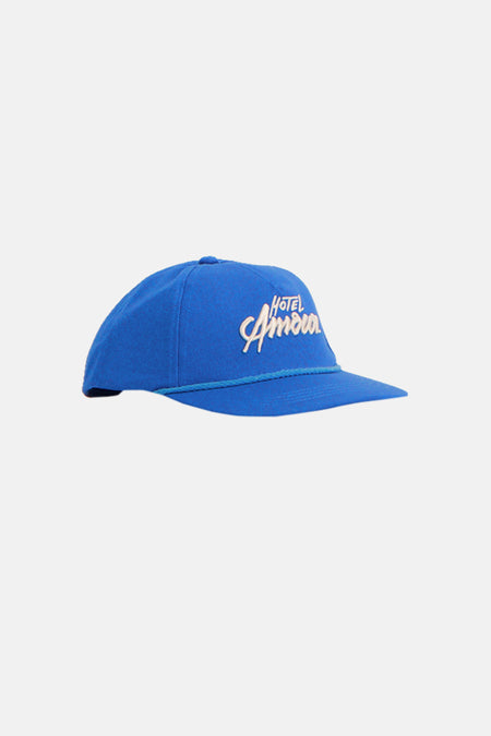 Blauwe pet van SELECTED, met geborduurd 'Hotel Amour' logo en koorddetail.
