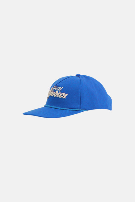 Blauwe pet van SELECTED, met geborduurd 'Hotel Amour' logo en een blauw koorddetail.
