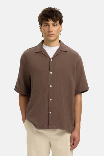Bruin overhemd met korte mouwen van SELECTED, gemaakt van textuurstof, met reverskraag en witte knopen, gedragen over een wit T-shirt en beige broek.