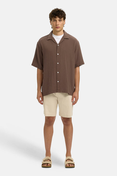 Bruin gestructureerd hemd met korte mouwen van SELECTED, gedragen over een wit T-shirt, gecombineerd met beige shorts en sandalen.