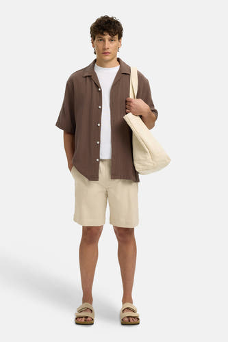 Bruin getextureerd hemd met korte mouwen van SELECTED met witte knopen, gedragen over wit T-shirt, met beige shorts, sandalen en draagtas.