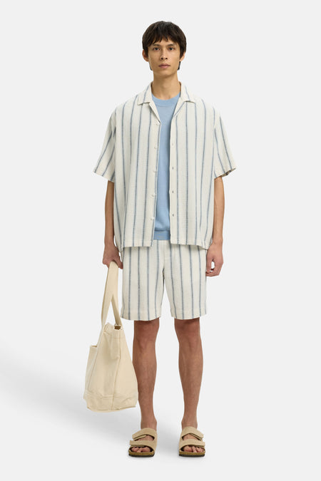 Ecru overhemd met korte mouwen van SELECTED, gestreept en gedragen over een blauw shirt, met bijpassende shorts en tas.