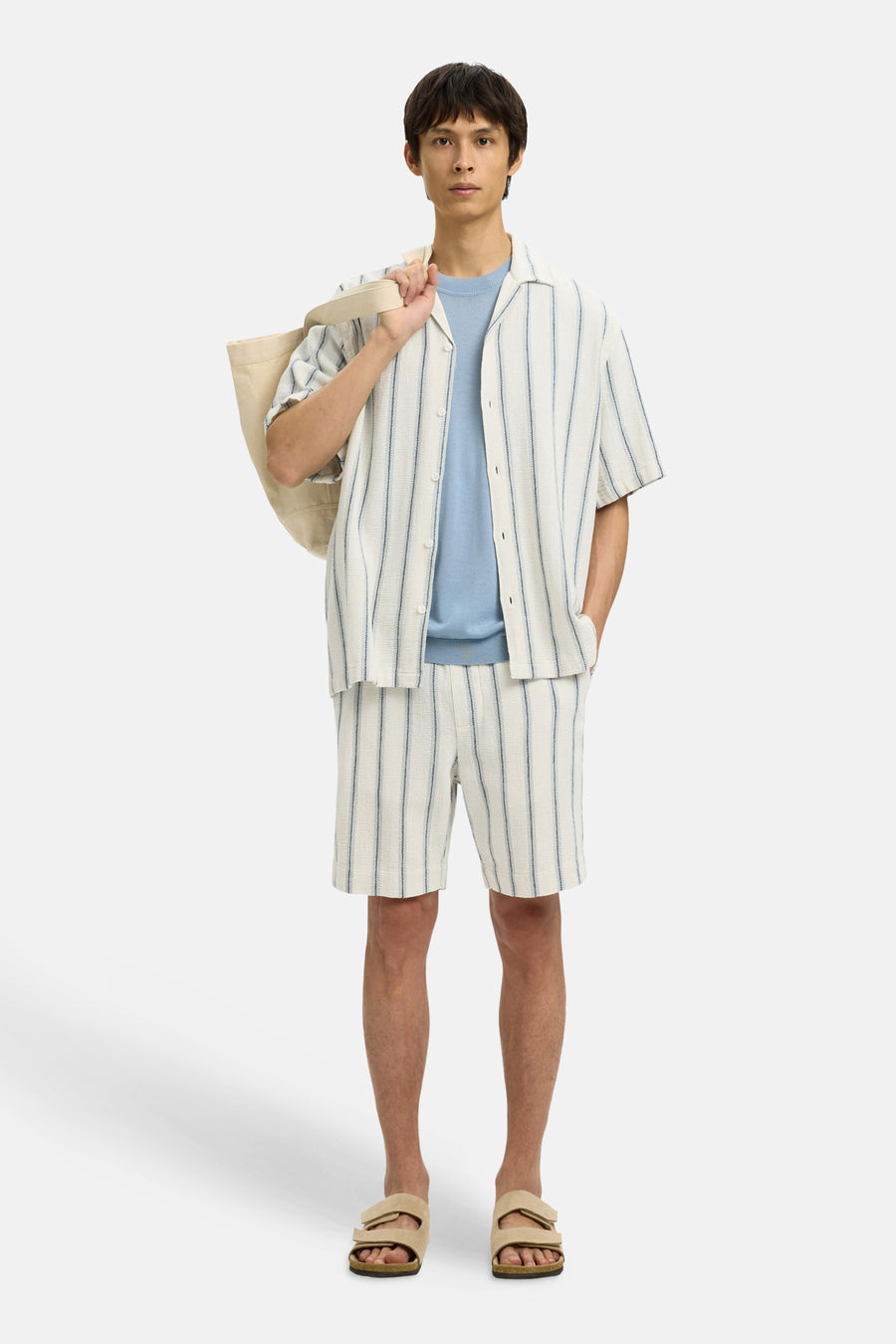 Ecru overhemd met korte mouwen van SELECTED, gestreept, gedragen over een lichtblauwe trui, met beige sandalen en een tas.