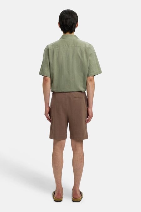 Bruine korte broek van SELECTED, achterkant, met fijne textuur en achterzak, model draagt groen overhemd en sandalen