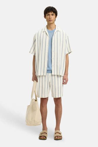 Ecru gestreepte korte broek van SELECTED, met blauwe strepen, gecombineerd met overhemd en lichtblauw shirt, model in lifestyle pose met canvas tas en sandalen
