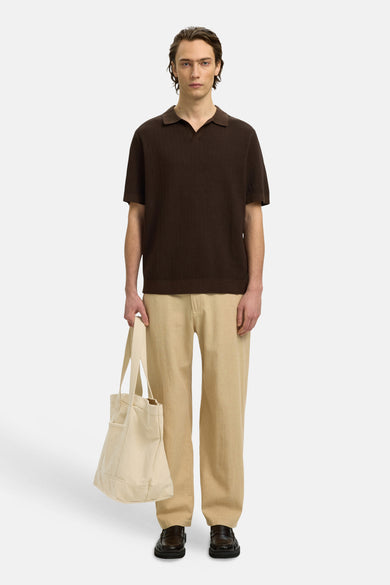 Polo marron de SELECTED, à manches courtes et avec un motif texturé subtil, combinée avec un pantalon beige et un sac en toile.