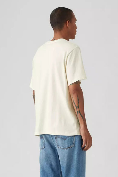 Ecru T-shirt met korte mouwen van Levi's®, met tatoeages op de armen, gecombineerd met een blauwe jeans.
