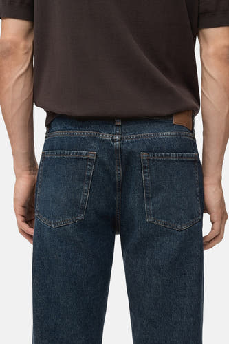 Slim jeans van donkerblauw denim van MANGO, achterkant, gecombineerd met een bruin T-shirt.
