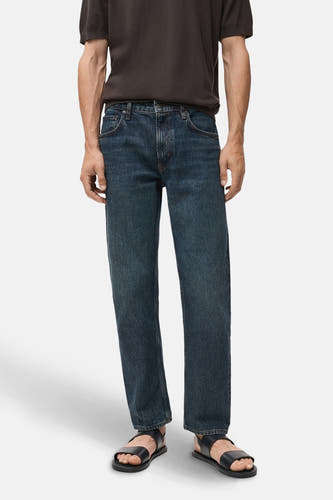 Slim jeans van donkerblauw denim van MANGO, gecombineerd met een bruin t-shirt en leren sandalen.