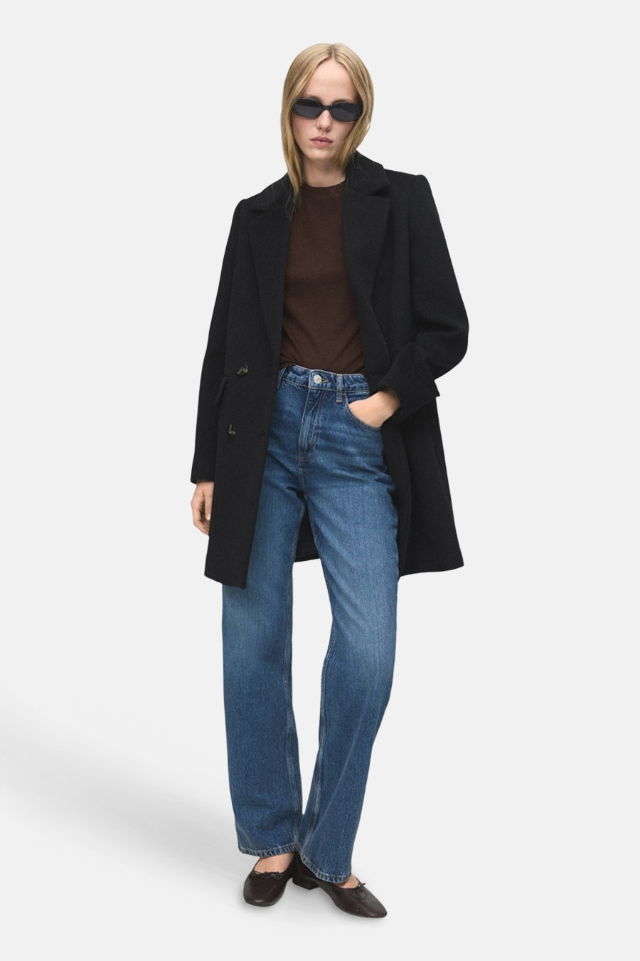 Zwarte jas van MANGO, met lange mouwen, gedragen over een bruine top en blauwe jeans.