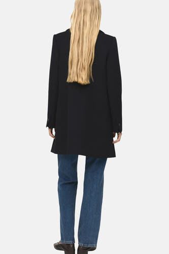Zwarte lange jas van MANGO, gezien van achteren, met blauwe jeans en zwarte schoenen.