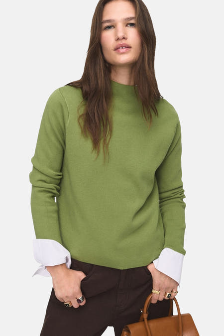 Groene trui met ronde hals van MANGO, met lange mouwen en witte overhemdmanchetten, gecombineerd met bruine broek.