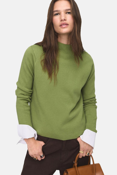 Groene trui met ronde hals van MANGO, met lange mouwen en witte overhemdmanchetten, gecombineerd met bruine broek.
