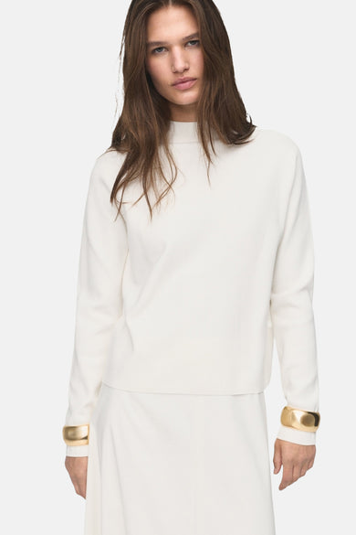 Pull blanc avec col rond de MANGO, avec des bracelets dorés et une longue jupe qui tombe.
