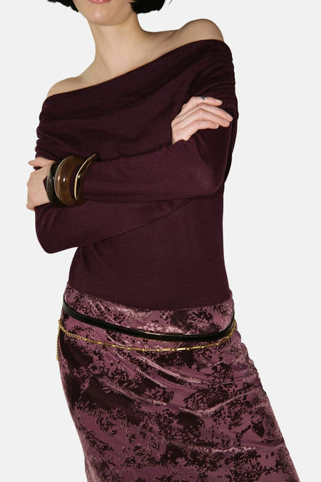 Bordeaux trui met ronde hals van MANGO, met lange mouwen, gedragen met een paarse rok met bloempatroon.
