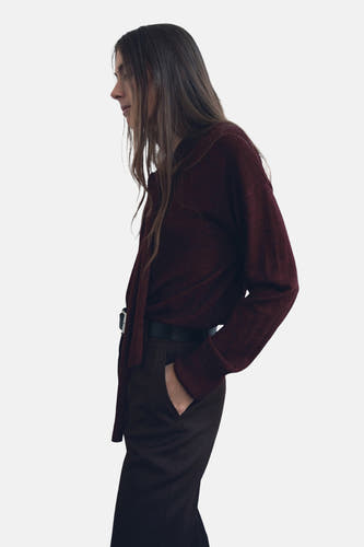 Bordeaux trui met ronde hals van MANGO, met lange mouwen en een strikdetail, gecombineerd met een donkere pantalon en riem.