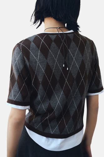 Multikleurige trui met ronde hals van MANGO, met argyle ruitpatroon en korte mouwen, gedragen over een wit T-shirt.
