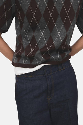 Multikleurige trui met ronde hals van MANGO, met argyle-ruitpatroon in bruin, grijs en wit, gedragen met een wit shirt en een donkere jeans.
