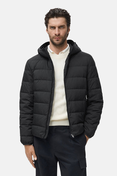 Manteau noir court de MANGO, avec capuche, porté sur une chemise blanche et un pantalon foncé.