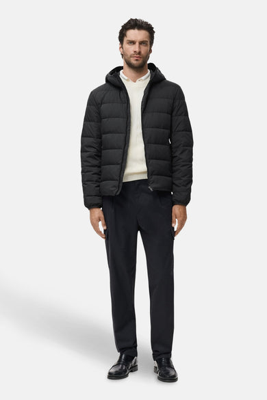 Manteau noir court de MANGO, avec capuche, porté sur une chemise crème et un pantalon foncé.
