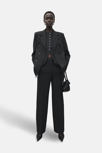 Pantalon gris de costume MANGO, combiné avec un blazer coordonné et une poche main noire.