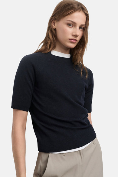 T-shirtue ble M colcol rond de deANGOANG, porté avec un un-shirt blanc, des short beige et des bottes en cuir noires.