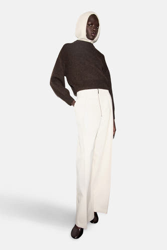Bruine trui met ronde hals van MANGO, gecombineerd met een witte broek en een wit muts.
