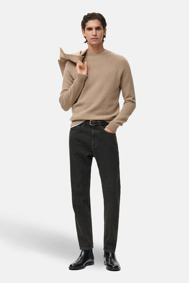 Beige trui met ronde hals van MANGO, gedragen met een jas over de schouder, donkere jeans en zwarte laarzen.