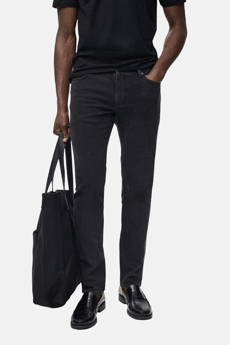 Donkergrijze slim fit jeans van MANGO, met een zwarte tas en zwarte leren schoenen.
