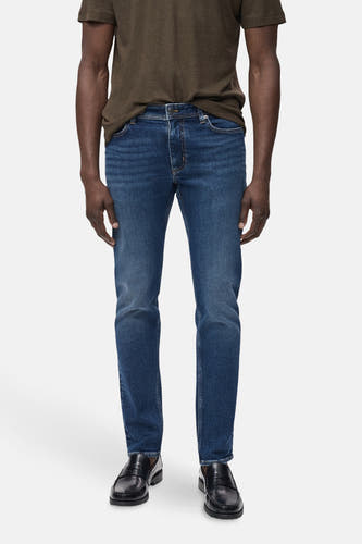 Slim jeans van MANGO in middenblauw denim, gecombineerd met een bruin t-shirt en zwarte loafers.