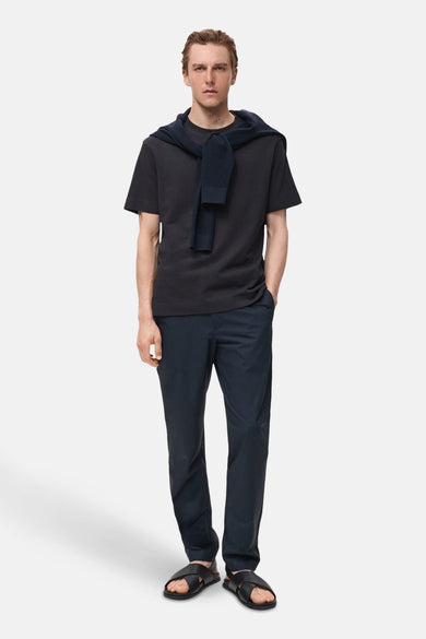 T-shirt bleu à manches courtes de MANGO, noué nonchalamment sur les épaules, associé à un pantalon foncé et des sandales.