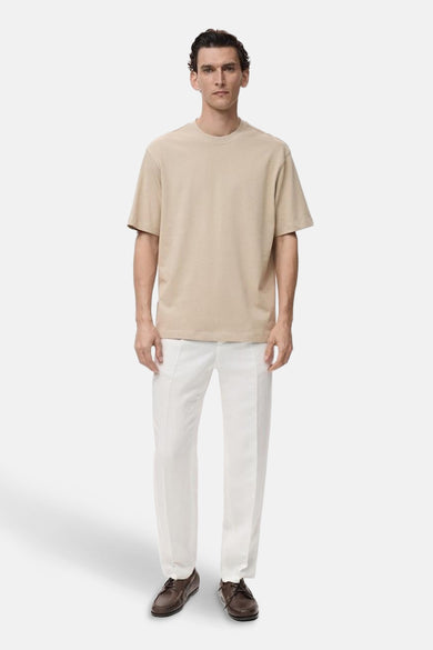 T-shirt beige à manches courtes de MANGO, associé à un pantalon blanc et des chaussures marron.