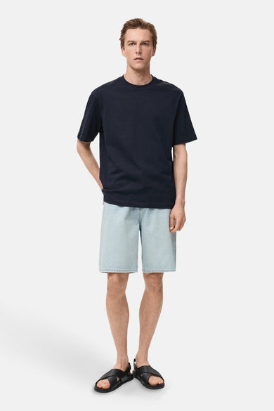 T-shirt bleu marine à manches courtes de MANGO, porté avec des shorts en denim et des sandales noires.