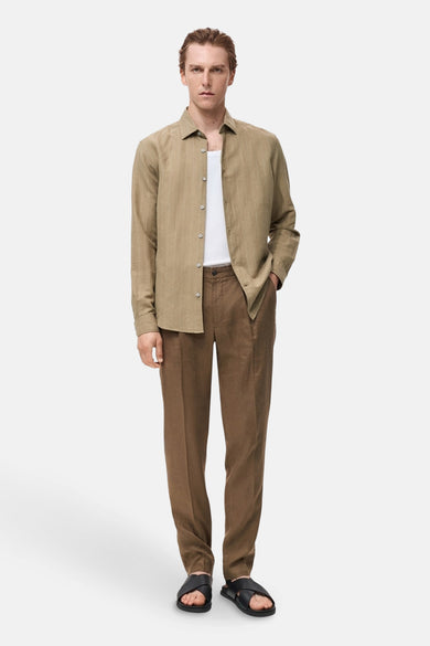 Kaki hemd met lange mouwen van MANGO, gedragen met een wit t-shirt en bruine pantalon met leren sandalen.